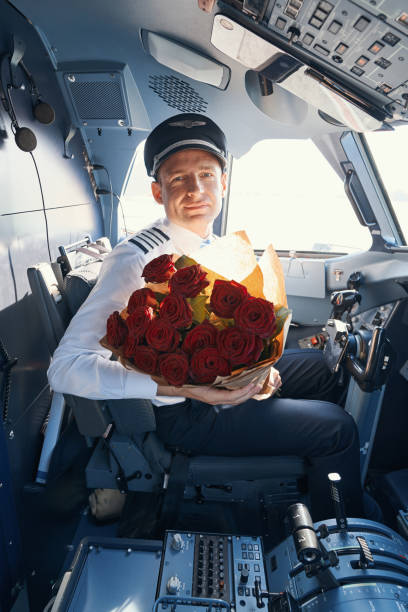 istock Man in pilot uniform sitting in airplane with roses 1357625089