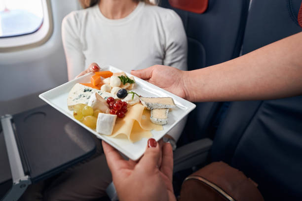 Airline stewardess giving plate with snacks to passenger Stewardess passing airline meal with cheese, grapes and vegetables to person in window seat airplane food stock pictures, royalty-free photos & images