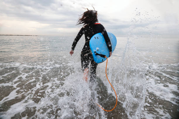 istock Female Surfer With Board Running Into Water 1357629752