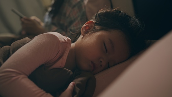 Attractive Cute Asian baby or child girl sleeping with her mother in the bedroom at night. She tired from playing all day. Mother is putting daughter to bed.
