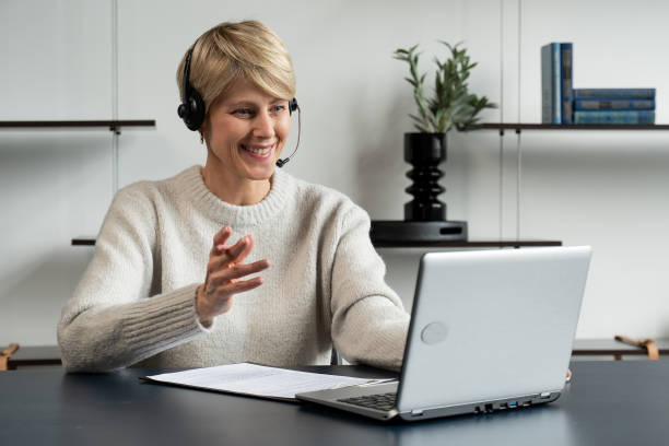 istock Smiling middle-aged modern woman wears a headset, a distance course, or training on a laptop 1357630107
