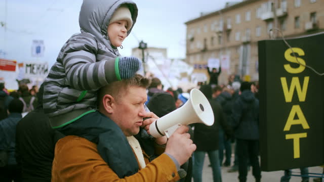 Dad, single parent, protesting with bullhorn. Boy sits on fathers shoulders.
