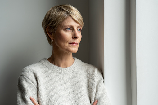 A thoughtful middle-aged woman looks out the window and is sad.