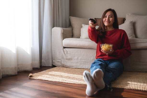 istock A beautiful young woman eating potato chips while searching channel with remote control to watch tv at home 1357631245