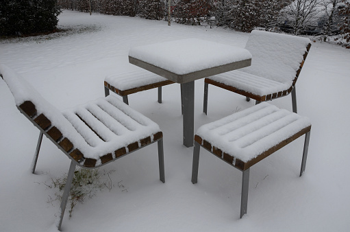 Park furniture chess table and chairs for four people made of light metal and wooden beams with backrest. on a bright snowy plain with bushes. covered with a layer of snow