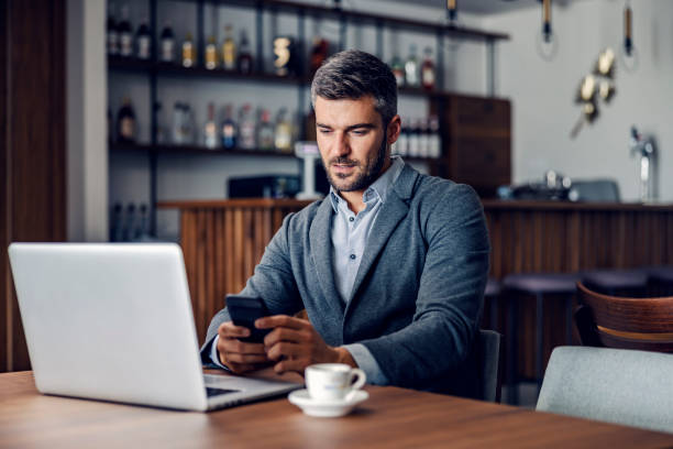istock A busy businessman is sitting in working friendly cafe and using his phone to read an important message from a client. There is a laptop on the table. A businessman texting while sitting in a cafe. 1357640148