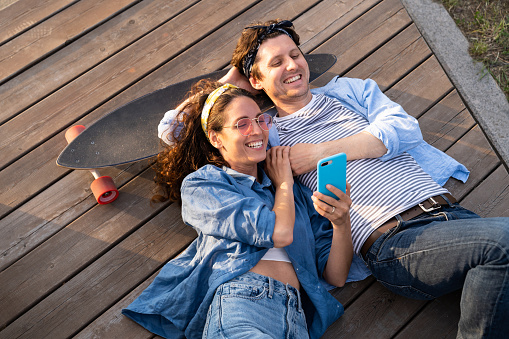 Vista superior de hombre y mujer con monopatín viendo videos o fotos en un teléfono inteligente photo