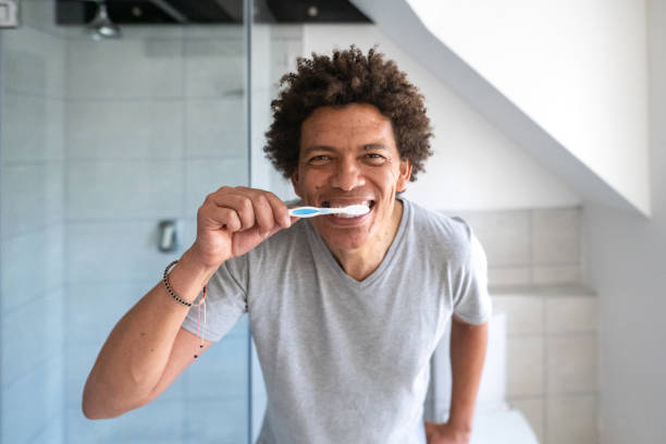 istock Male with funky hair tooth brushing routine in a bathroom brushing teeth looking in mirror 1357643770
