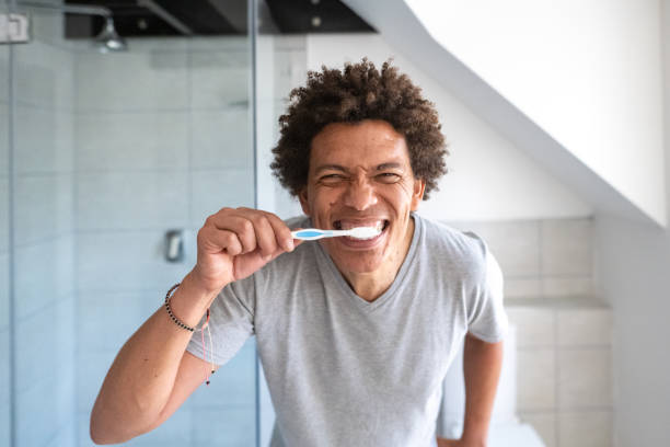 istock Male with funky hair tooth brushing routine in a bathroom front teeth brushing looking in mirror 1357644645