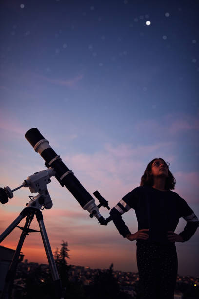 istock Girl with astronomical telescope stargazing under twilight sky. 1357645904