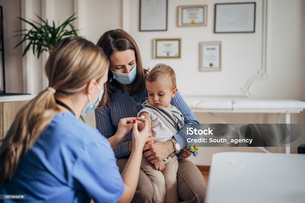 Little boy getting vaccinated Three people, female doctor vaccinating a little boy who is with his mother, they are in the pediatrician's office. Doctor Stock Photo