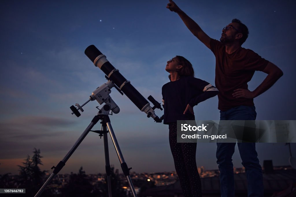 Silhouettes of father, daughter and astronomical telescope under starry skies. Astronomy Stock Photo