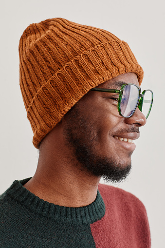 Vertical side view portrait of smiling African-American man wearing knit hat and sweater