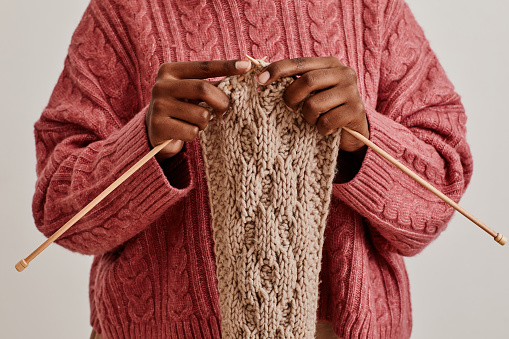 Close up of young African-American woman knitting scarf and wearing cozy sweater, copy space