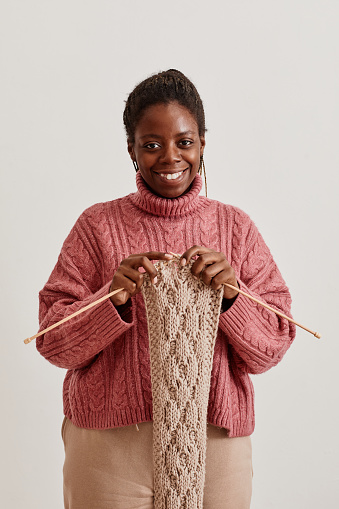 Minimal waist up portrait of young African-American woman knitting scarf and smiling at camera