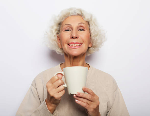 istock old excited lady smiling laughing, holding cup drinking coffee, tea, over white background 1357648290