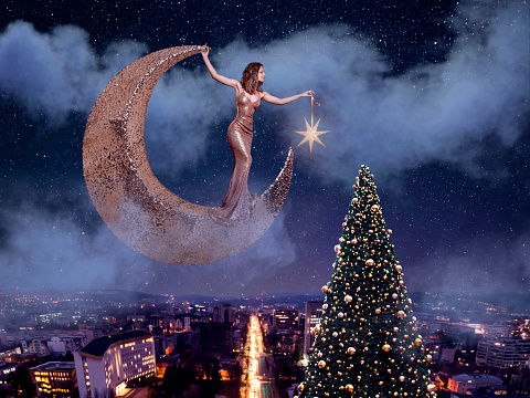 Beautiful woman stands on the moon and hangs a star on the christmas tree