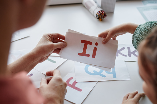 Close-up of child learning English letters with cards together with teacher at the table