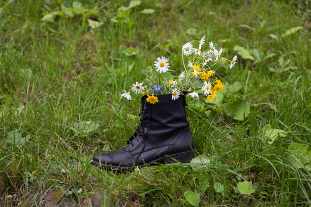 Colorful summer flowers in black leather boot on green grass. Creative flowers design for home or business. Poster for flowers shop. Environmental movement concept. Carbon print concept with shoe.