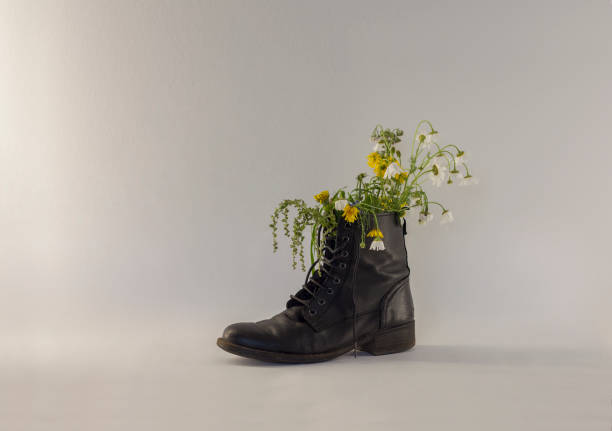Flowers and grass in black old boot on white background.