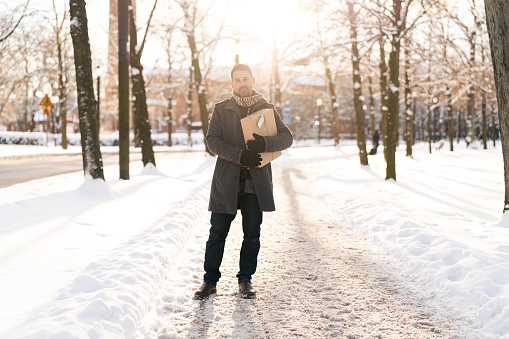Man with a Christmas gift under his arm is walking through a city covered in snow on a beautiful sunny winter day.