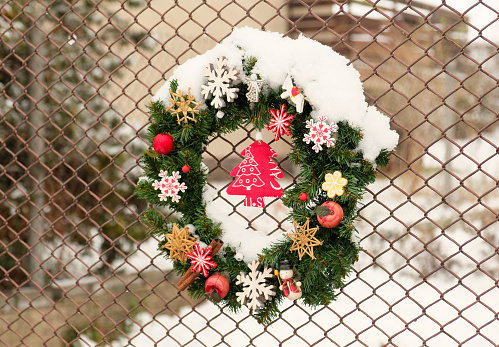 Decorative Christmas wreath made of fir branches is decorated with snowflakes, stars, apples, cinnamon, wooden toys. A traditional Christmas wreath creates a festive mood in anticipation of the holiday. Outdoor Christmas decor.