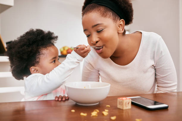 tiro de uma menina alimentando sua mãe cereal - cereais de pequeno almoço - fotografias e filmes do acervo