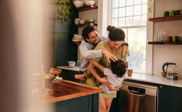Parents playing with their son in the kitchen. Two happy parents laughing and having fun with their young son at home. Family of three spending some quality time together.