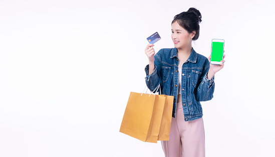 Excited smile Asian woman holding shopping bag show credit card using smartphone payment banking shopping online. Happiness lady paying debit electronic card for shopping advertising. Finance concept.