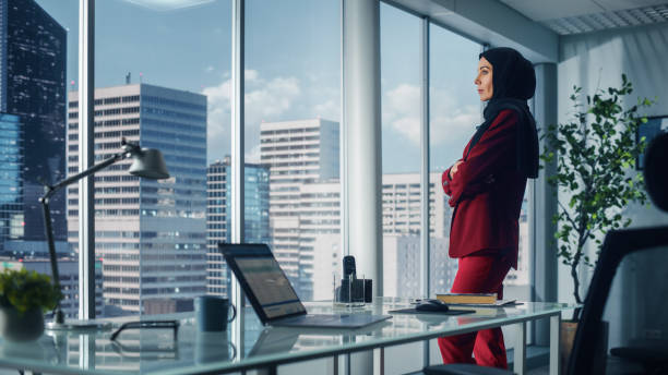 Successful Muslim Businesswoman Wearing Suit and Burka Standing in Office Looking out of Window on Big City. Confident Female Digital Entrepreneur Planning Investment Strategy for e-Commerce Startup Successful Muslim Businesswoman Wearing Suit and Burka Standing in Office Looking out of Window on Big City. Confident Female Digital Entrepreneur Planning Investment Strategy for e-Commerce Startup middle east stock pictures, royalty-free photos & images
