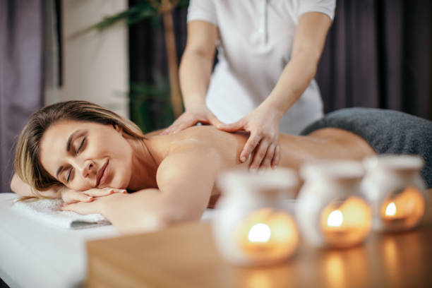 Attractive young woman receiving relax back massage Beautiful young woman receiving relaxation back massage in spa salon. She has a nice healthy skin and looks beautiful and very attractive. Candles with ethereal oil are on the desk in front of her massage stock pictures, royalty-free photos & images