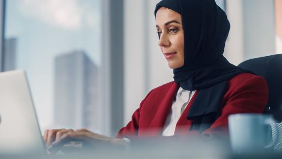 Retrato en primer plano de una hermosa mujer de negocios musulmana con burka sentada en su escritorio trabajando en una computadora portátil en la oficina. Exitosa estrategia de inversión del plan de CEO corporativo para una startup de comercio electrón photo