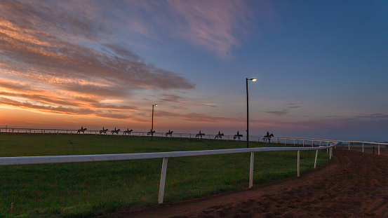 Horses riders early dawn morning exercise training a walking around sand track silhouetted a scenic panoramic lifestyle landscape