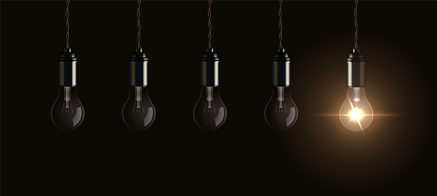 Light bulbs hang from ceiling with one bright lightbulb glowing, symbol of innovation