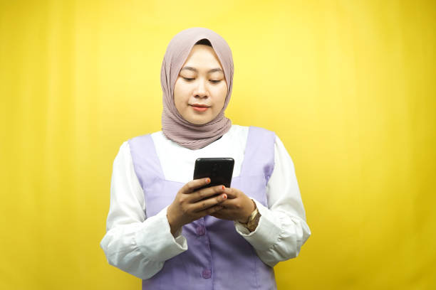 Beautiful asian young Muslim woman holding smartphone isolated on yellow background stock photo
