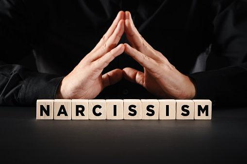 Man with clasped hands with the word narcissism on wooden blocks. Personal ego or selfishness concept.