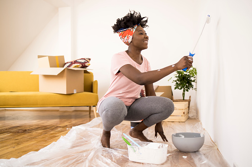 Happy African American woman painting walls in her new house.