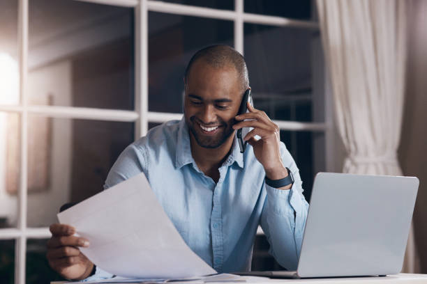 istock Shot of a young businessman reading paperwork while making a phone call using his smartphone 1357669646