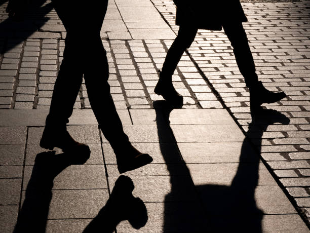 istock Two anonymous unrecognizable people walking through the street, dark black leg silhouettes, shadows. Pedestrians outdoors, society, anonymity, loneliness and sadness, social issues abstract concept 1357670710