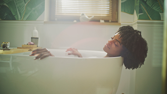 Woman lying in a bathtub, relaxing in hot water. Profile view