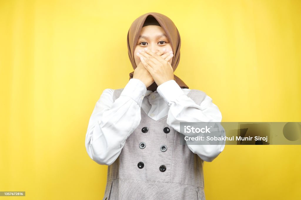 Beautiful young asian muslim woman shocked, surprised, disbelieving, getting shocking information, with hands covering mouth isolated on yellow background 20-24 Years Stock Photo