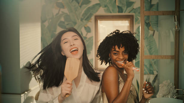 Feeling fabulous. Diverse friends enjoying morning bathroom routine and having fun in front of mirror. Crazy dance moves
