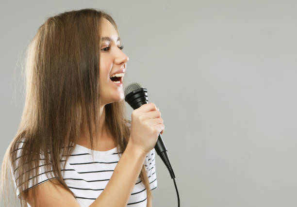 istock Beauty model girl singer with a microphone over light grey background 1357676001