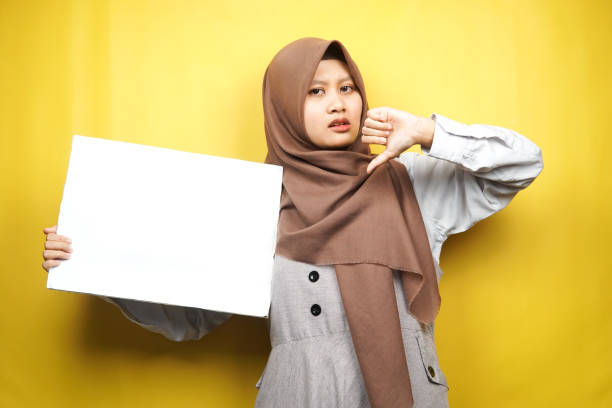 Pretty young muslim woman dislike hand, holding blank empty banner, placard, white board, blank sign board, white advertisement board, presenting something in copy space, promotion stock photo