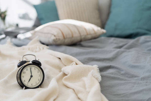 istock Black analog alarm clock standing on bed 1357679481
