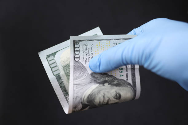 istock Gloved hand holds hundred dollar bill closeup 1357680094