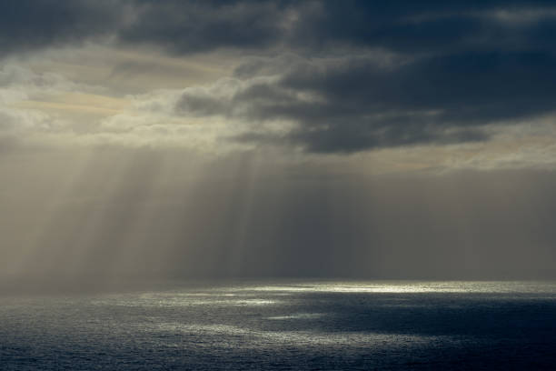 istock Rays of sun through dark clouds at ocean. 1357684278