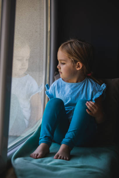 istock Little girl sitting down by the window while watching through the window 1357685037