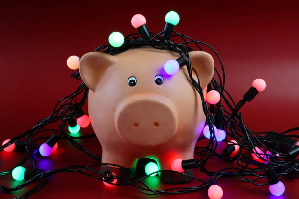 赤い表面に照らされた弦の妖精のライトで丸く包まれた貯金箱のクローズアップ画像は、前景、クリスマス予算、手形、負債、財政コンセプトに焦点を当てています - focus on foreground tax close up finance ストックフォトと画像