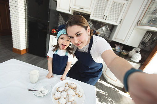 Mom and her daughter bake cookies at home in the modern kitchen and making selfie